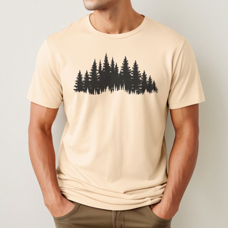 May include: A beige t-shirt with a black silhouette of a forest on the front.