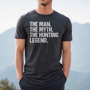 May include: A dark heather grey t-shirt with the text "THE MAN. THE MYTH. THE HUNTING LEGEND." printed in white.