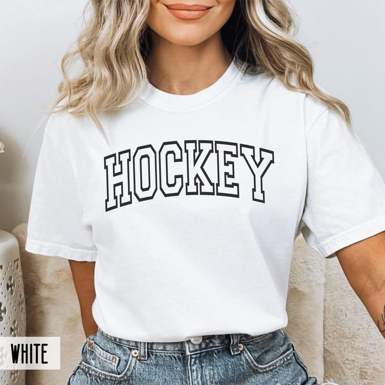 A woman wearing a white t-shirt with black block lettering spelling HOCKEY.
