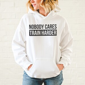 Pu&ograve; includere: Felpa con cappuccio bianca con il testo "Nobody Cares Train Harder" in nero.