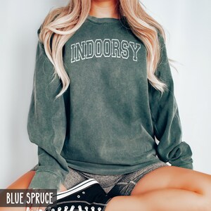 Pode incluir: Uma camisola verde escura com a palavra "INDOORSY" impressa em branco na frente. A camisola &eacute; feita de um material macio e confort&aacute;vel e tem um caimento descontra&iacute;do.