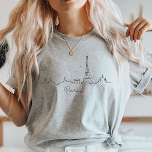 Op de afbeelding: Een grijs T-shirt met een zwarte lijntekening van de Eiffeltoren en het woord "Paris" eronder.