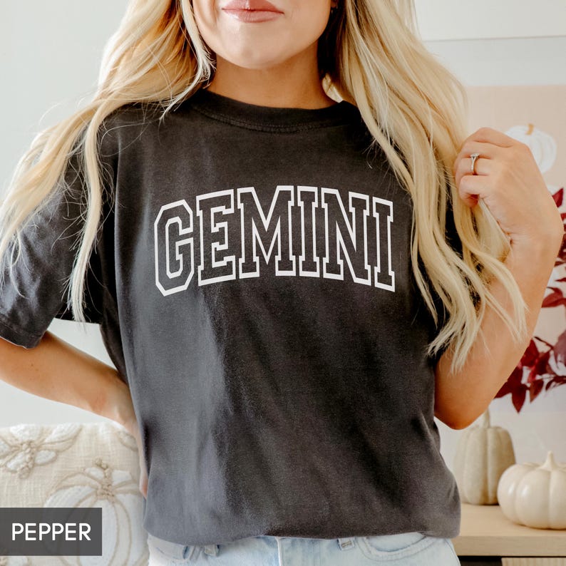 May include: A dark gray t-shirt with the word "GEMINI" in white, block letters. The shirt has a vintage, slightly faded look. The shirt is a casual, everyday wear item.