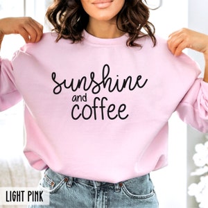 May include: A light pink sweatshirt with the text "sunshine and coffee" in black lettering.