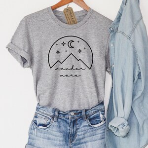 A heather gray t-shirt with a black mountain graphic is displayed alongside blue denim shorts and a light blue denim shirt.
