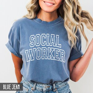 Puede incluir: Una camiseta azul vaquero con texto blanco que dice "SOCIAL WORKER" en una fuente universitaria.