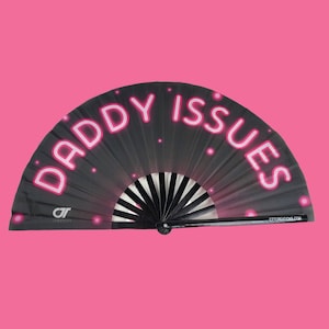 May include: Black folding fan with a pink neon design that says "Daddy Issues". The fan has a black handle and a white logo that says "CT Creations".