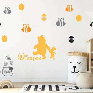 May include: A Winnie the Pooh themed nursery decor with a yellow Winnie the Pooh and Piglet silhouette, a honey pot with bees, and the name "Winston" written in grey. The nursery also features a white rabbit toy sitting on a wooden stool, a grey and white storage basket, and a wooden dollhouse.