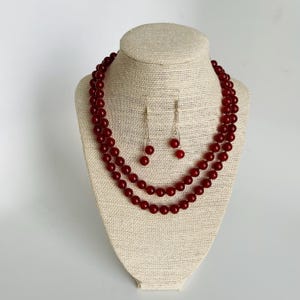 May include: A red carnelian gemstone necklace and earrings set. The necklace is a double strand of round beads. The earrings are simple drop earrings with a single round bead.