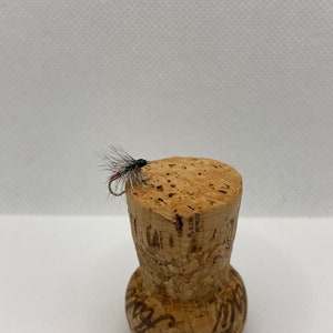 May include: A black and red fly fishing lure with silver tinsel and a black bead head, tied on a cork.