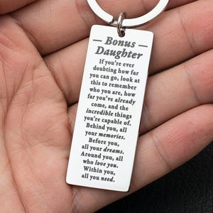 May include: A silver-toned rectangular metal keychain featuring an engraved message that reads: Bonus Daughter. If you're ever doubting how far you can go, look at this to remember who you are, how far you've already come, and the incredible things you're capable of.