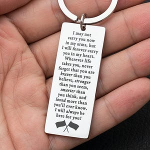May include: Silver-colored rectangular keychain with a circular ring. The keychain has engraved text: "I may not carry you now in my arms, but I will forever carry you in my heart... I will always be here for you!" Two small flags are at the bottom.