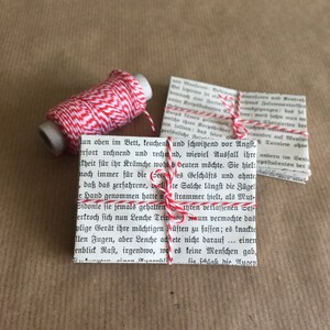 Puede incluir: Una bobina de hilo de panadero rojo y blanco est&aacute; envuelta alrededor de una peque&ntilde;a pila de libros de bolsillo antiguos. El hilo est&aacute; atado con un lazo alrededor de los libros.