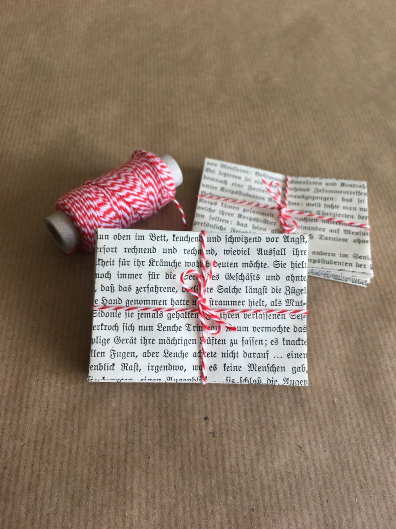 Puede incluir: Una bobina de hilo de panadero rojo y blanco est&aacute; envuelta alrededor de una peque&ntilde;a pila de libros de bolsillo antiguos. El hilo est&aacute; atado con un lazo alrededor de los libros.