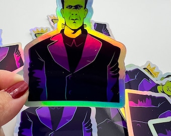 May include: A stack of iridescent holographic stickers featuring a green-skinned monster wearing a gold crown and a black suit. The monster has a serious expression and is looking directly at the viewer.