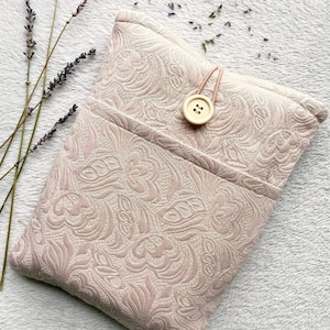 May include: A pink fabric pouch with a floral pattern and a button closure. The pouch is lying on a white fluffy surface with dried lavender flowers scattered around it.