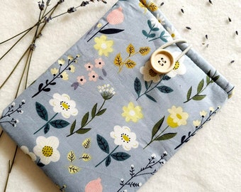 Puede incluir: Una bolsa de tela azul claro con un patrón floral. La bolsa tiene un cierre de botón y un lazo para una correa. La bolsa está sobre una superficie blanca con ramitas de lavanda secas.