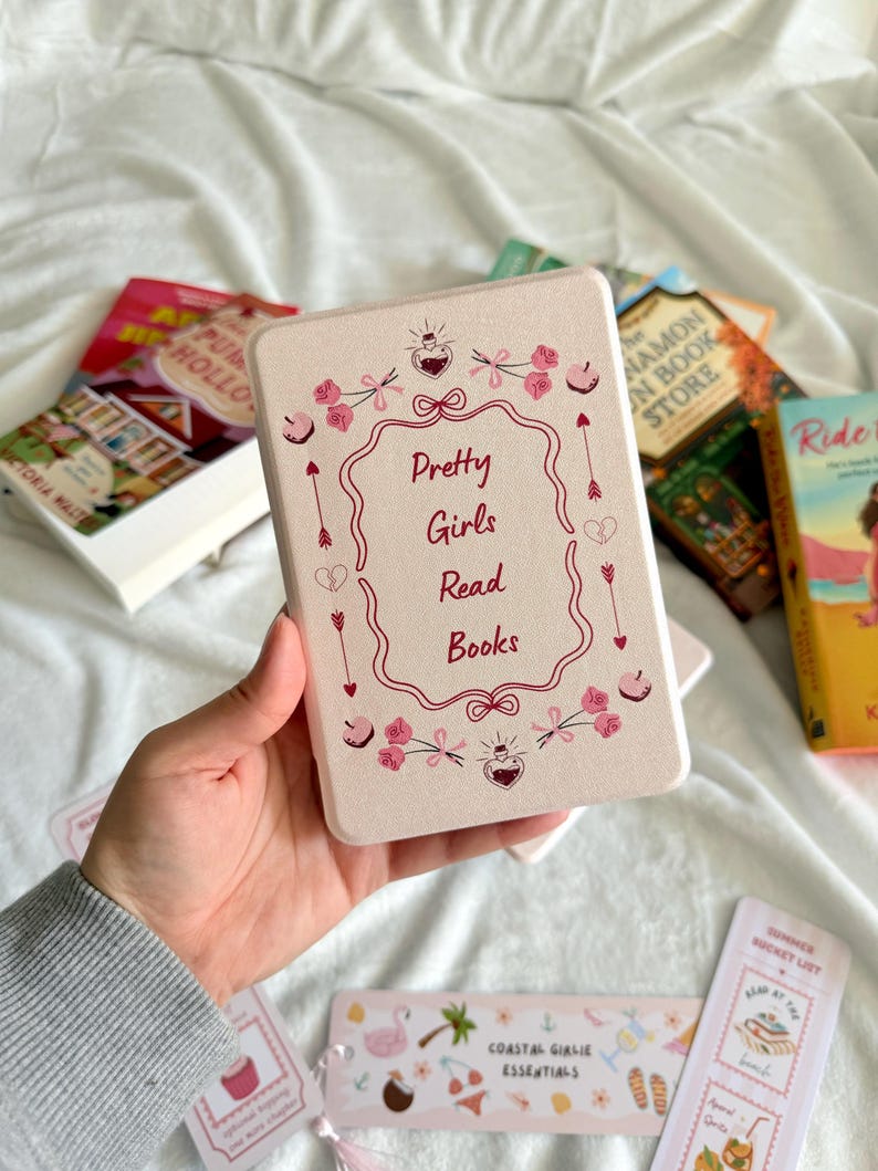 May include: A rectangular, light pink book box with the text "Pretty Girls Read Books" in a decorative frame. The box is surrounded by pink floral and arrow designs. Several books and bookmarks are visible.