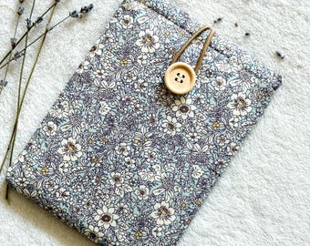 Puede incluir: Una pequeña bolsa de tela azul con un estampado floral y un cierre de botón marrón. La bolsa está sobre una superficie blanca y esponjosa.