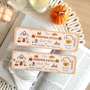 May include: Two rectangular paper bookmarks with rounded corners featuring a cream background and orange text reading The PUMPKIN PATCH Book Club. The design includes illustrations of houses, pumpkins, pies, and a mug with the text Spicy Latte Provided.