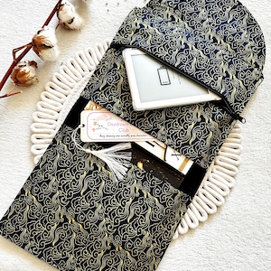 May include: A black and gold fabric pouch with a zipper closure. The pouch has a pattern of swirling clouds and is designed to hold an e-reader. The text "Daydream Club" is visible on a tag attached to the pouch.