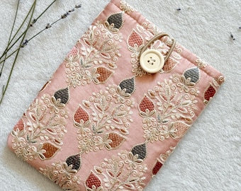Puede incluir: Una bolsa de tela rosa con un patrón floral y un cierre de botón blanco. La bolsa está hecha de una tela suave y texturizada y tiene un brillo sutil.