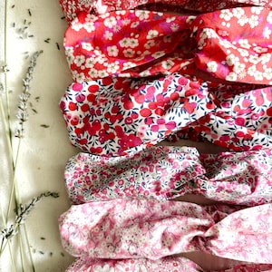 May include: A collection of floral headbands in various shades of red and pink. The headbands feature different patterns, including small white flowers and cherry-like designs. The fabric appears soft and the headbands are twisted at the top.