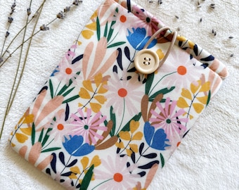 May include: A floral print book cover with a wooden button closure. The cover features a white background with pink, blue, yellow, and green flowers. Dried lavender sprigs are placed near the cover.
