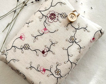 Könnte beinhalten: Eine weiße Stofftasche mit einem floralen Stickmuster in schwarzem, rosa und goldenem Garn. Die Tasche hat einen Verschluss aus Holzknopf.