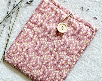 Puede incluir: Una bolsa de tela rosa con un estampado floral blanco y un cierre de botón de madera. La bolsa está sobre una superficie blanca y peluda.