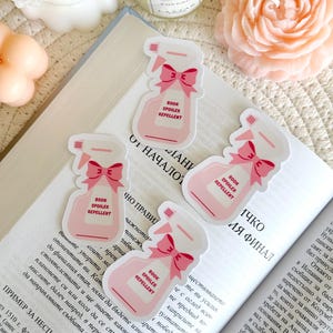 Op de afbeelding: Vier roze en witte stickers met een cartoonillustratie van een spuitfles met een roze strik en de tekst "Book Spoiler Repellent".