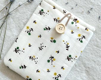 Puede incluir: Bolsa de tela blanca con un patrón floral en amarillo y verde. La bolsa tiene un cierre de cordón marrón y un botón de madera.