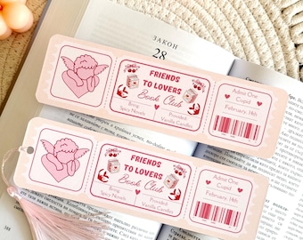 May include: Two rectangular paper bookmarks designed as event tickets with pink borders and text. Each features a pink cupid illustration, the text "Friends to Lovers Book Club", "Admit One Cupid February 14th", and a barcode. One has a pink tassel.