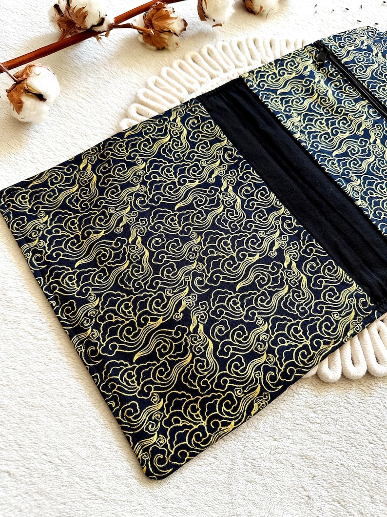 May include: Black zippered pouch with a gold cloud pattern. The pouch is made of fabric and has a zipper closure.