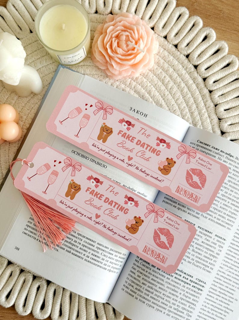 May include: Two rectangular pink bookmarks featuring illustrations of champagne glasses, bows, and teddy bears. The text reads The FAKE DATING Book Club, We're just playing a role, right? No feelings involved?, and Admit One Twisted Liar. Each bookmark has a pink tassel.