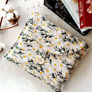 May include: A beige fabric clutch with a floral pattern of white daisies and green stems. The clutch has a flap closure with a button and a loop.