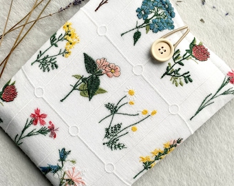 May include: White fabric pouch with a floral embroidery design. The pouch has a button closure and a gold metal clasp.