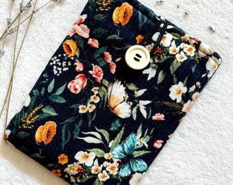 Puede incluir: Una bolsa de tela negra con estampado floral y de mariposas. La bolsa tiene un cierre de botón y una correa elástica negra.