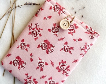 Puede incluir: Una funda de teléfono de tela rosa con un estampado floral rojo y un cierre de botón de madera.
