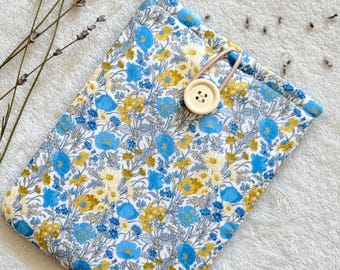 Puede incluir: Una bolsa de tela blanca con un estampado floral azul y amarillo. La bolsa tiene un cierre de botón de madera y un cordón marrón.