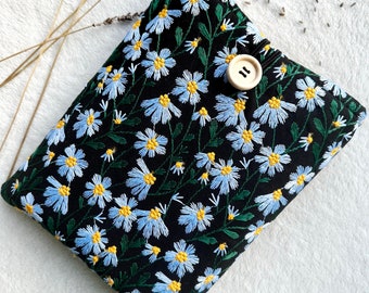 May include: A black fabric clutch with a floral pattern embroidered in blue and yellow. The clutch has a wooden button closure.