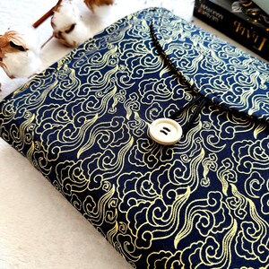 May include: A black fabric book cover with a gold cloud pattern and a white button closure.