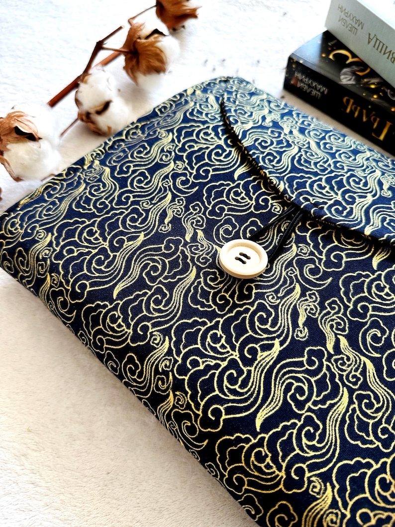 May include: A black fabric book cover with a gold cloud pattern and a white button closure.