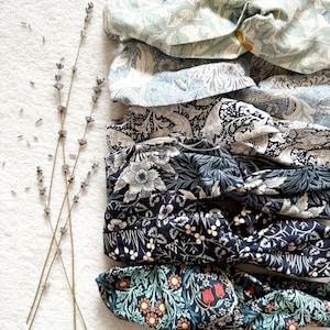 May include: Five fabric headbands with floral patterns in shades of blue and green. The headbands are arranged in a stack, with the top headband being a light blue and green floral pattern, followed by a darker blue and white floral pattern, then a dark blue and white floral pattern, then a dark blue and white floral pattern, and finally a dark green and white floral pattern.