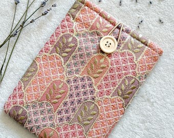 Puede incluir: Una funda para teléfono bordada en rosa y dorado con cierre de botón. La funda tiene un patrón floral y está hecha de una tela suave.