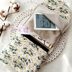May include: A white canvas pouch with a zipper closure and a daisy floral embroidery design. The pouch is open and a white e-reader is inside. The e-reader screen displays the text "Follow Her Down" and the author's name.