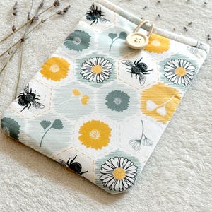 May include: A small, light blue fabric pouch with a yellow and green floral pattern and bees. The pouch has a wooden button with the number 23 on it.