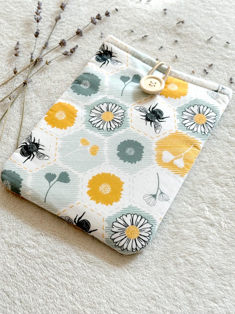May include: A small, light blue fabric pouch with a yellow and green floral pattern and bees. The pouch has a wooden button with the number 23 on it.