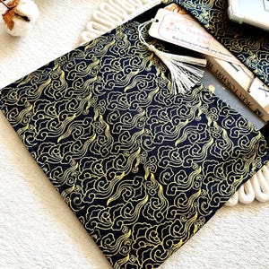 May include: A black fabric book sleeve with a gold cloud pattern. The sleeve has a tassel and a bookmark that says "Daydream Club".