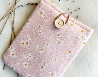 May include: A light pink, rectangular case with a daisy pattern. The case has a button closure and a loop. The daisies are white with yellow centers. The case is made of a soft, quilted fabric. Dried lavender sprigs are in the background.